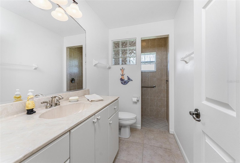 Guest bath has a walk in shower, tiled flooring, and long vanity w/cultured marble top.