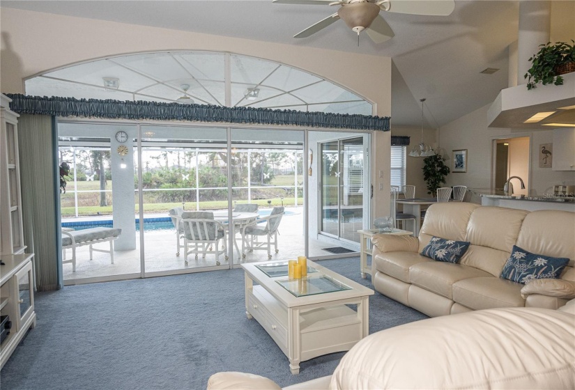 Living room with a wall of windows and soaring ceilings. Views of the pool area.