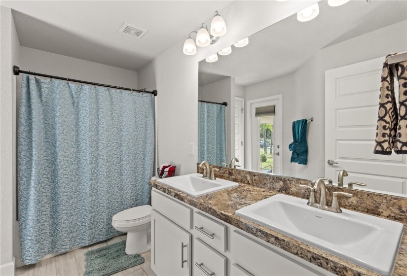 Guest bathroom #2 featuring dual vanities, alcove tub, and direct access to the screened-in lanai.